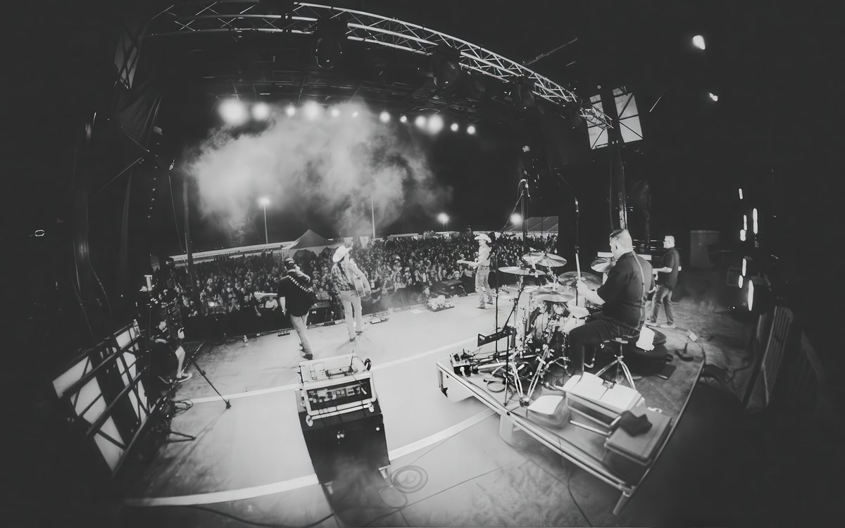 Festival stage viewed from behind the drum kit, crowd stretching into the dark
